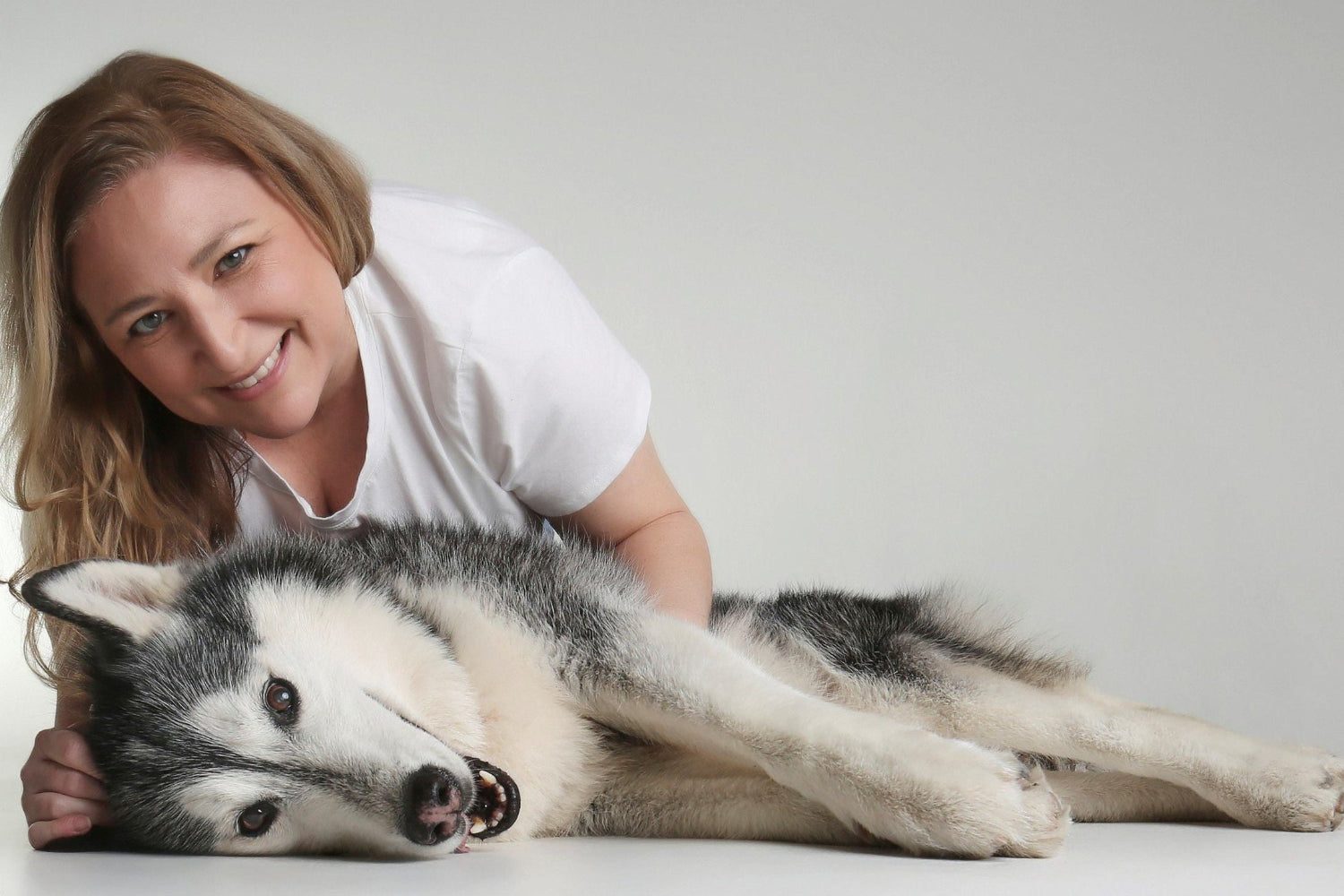 Woman lying next to a dog on a plain background